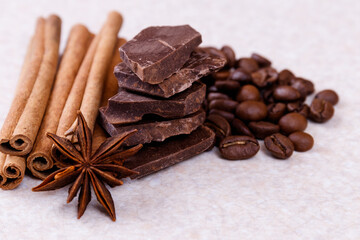 Stack of chocolate bar pieces with heap of roasted coffee beans and spices, cinnamon sticks and...