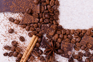 Pieces of chocolate bar on a white table with roasted coffee beans and spices, cinnamon sticks and anise stars, covered with cocoa powder. Copy space in the corner in square form. Top view.