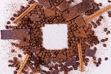Pieces of chocolate bar on a white table with roasted coffee beans and spices, cinnamon sticks and...