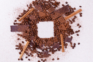 Pieces of chocolate bar on a white table with roasted coffee beans and spices, cinnamon sticks and...