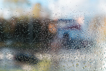 Raindrops on glass, street in the background is blurred. Close-up window after rain, on a sunny day