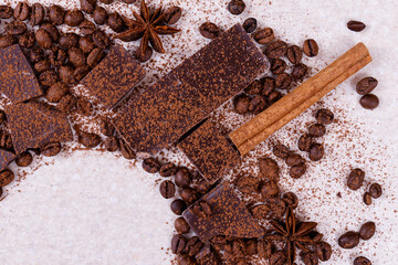 Pieces of chocolate bar on a white table with roasted coffee beans and spices, cinnamon sticks and anise stars, covered with cocoa powder. Copy space in the corner in circle form. Top view.