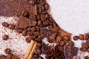 Pieces of chocolate bar on a white table with roasted coffee beans and spices, cinnamon sticks and...