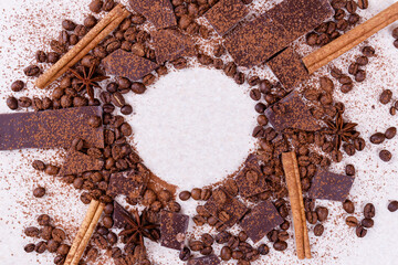 Pieces of chocolate bar on a white table with roasted coffee beans and spices, cinnamon sticks and...