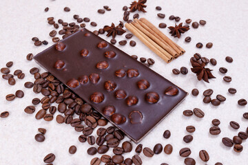 Chocolate bar with nuts on a white table with coffee beans and spices. Roasted coffee beans, cinnamon sticks and anise stars. Chocolate bar with hazelnuts. 