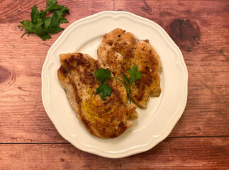 Pan seared chicken cutlets on white plate over wooden background.