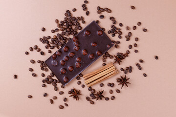 Chocolate bar with nuts on the beige background with coffee beans and spices. Roasted coffee beans, cinnamon sticks and anise stars. Chocolate bar with hazelnuts. Top view.