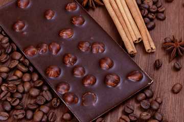 Chocolate bar with nuts on a wooden table with coffee beans and spices. Roasted coffee beans, cinnamon sticks and anise stars. Chocolate bar with hazelnuts. 