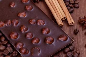 Chocolate bar with nuts on a wooden table with coffee beans and spices. Roasted coffee beans, cinnamon sticks and anise stars. Chocolate bar with hazelnuts. 