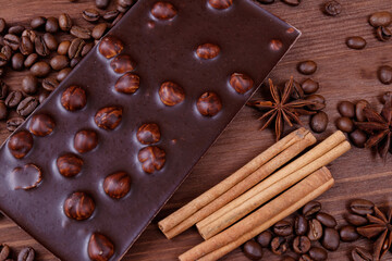 Chocolate bar with nuts on a wooden table with coffee beans and spices. Roasted coffee beans, cinnamon sticks and anise stars. Chocolate bar with hazelnuts. 