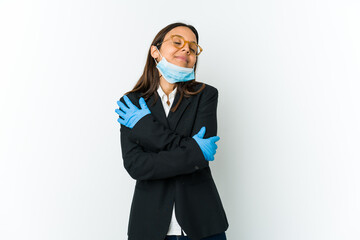 Young business latin woman wearing a mask to protect from covid isolated on white background hugs, smiling carefree and happy.