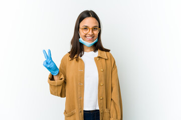 Young latin woman wearing a mask to protect from covid isolated on white background showing victory sign and smiling broadly.