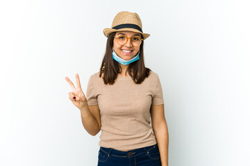 Young latin woman wearing hat and mask to protect from covid isolated on white background showing number two with fingers.