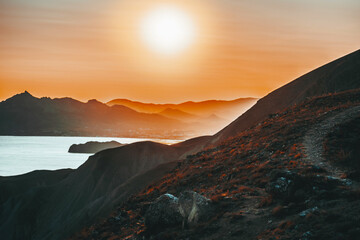 Plakat Hilly landscape by the sea in a bright orange sunset. Layers of mountains at sunset, background image