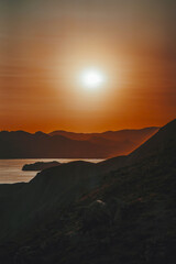 Hilly landscape by the sea in a bright orange sunset. Layers of mountains at sunset, background image