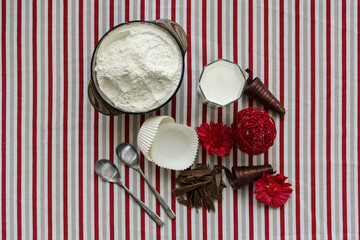 Ingredients for baking cupcakes - flour, milk, chocolate. White paper molds on the tablecloth with grey, red and white stripes. Preparing process to baking. Top view.