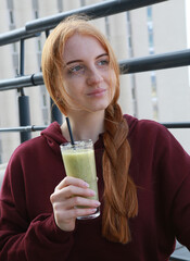 A girl sits and holds a glass of smoothie in her hand