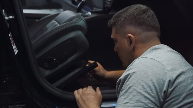 Professional male mechanic in uniform fixing seat inside modern dark car. Concept of car assembly. Working process at garage.