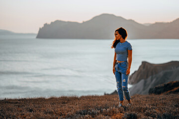 Picturesque mountain landscape at sunset with the sea on the horizon, a young beautiful woman walks down the slope in the orange rays of the sunset
