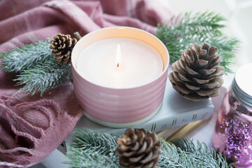 Aromatic burning candle, fir branches, cones and pink plaid. Christmas background. Soft focus.