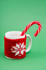 candy cane in cup with knitted cup holder with snowflake on green background