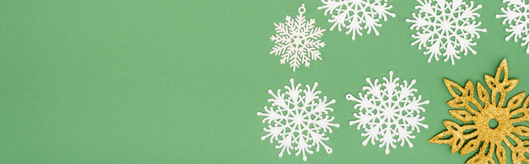 panoramic crop of decorative white and golden snowflakes on green background with copy space
