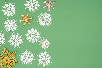 top view of decorative white, golden and silver snowflakes on green background with copy space