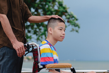 Obraz premium Asian special child on wheelchair is smiling, playing and doing activity on the sea beach, Lifestyle of disability child, Life in the education age, Happy disabled kid in travel holidays concept.