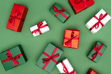 top view of multicolored gift boxes with red ribbons on green background