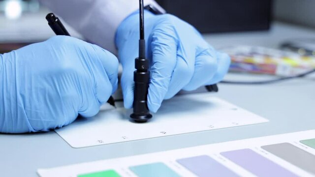 Close up of Hands with blue gloves on a laboratory desk, imprints and writes color code on plastic board. Powder factory laboratory process with color charts and industrial equipments. Slow motion.