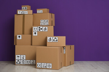 Cardboard boxes with different packaging symbols on floor near purple wall, space for text. Parcel delivery