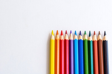 Line of colored pencils on isolated white background. Empty space for text or signature. Drawing supplies with assorted colors on the school white table, top close up view. Pencils from bottom