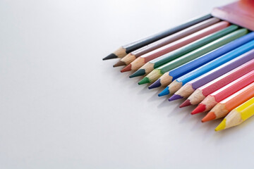 Naklejka premium New multicolored pencils peeking out of a box, positioned on a white table with a signature area. Bright colors. Shadow from the slates.