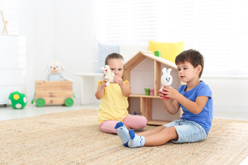 Cute little children playing with toys near wooden house on floor at home