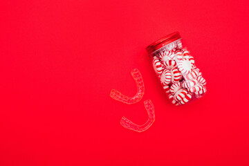 Invisible braces and a jar of candies on red background. Holiday invisible aligners flat lay.