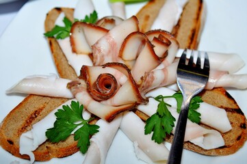 Plate with smoked bacon beautifully laid on fried bread with veins of meat, lard with greens for a snack, Close-up
