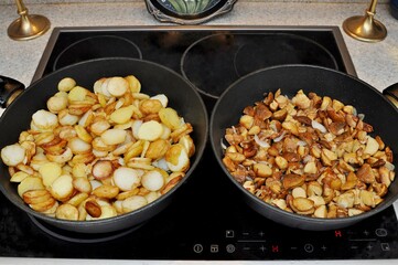 Delicious potato slices and mushrooms with onions fried in two pans on an electric stove for a family dinner