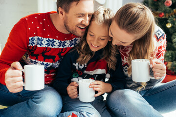 happy family in sweaters holding cups with drinks on christmas