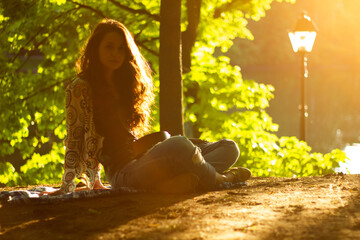 beautiful girl sits in the park near the trees and plays the musical instrument ukulele