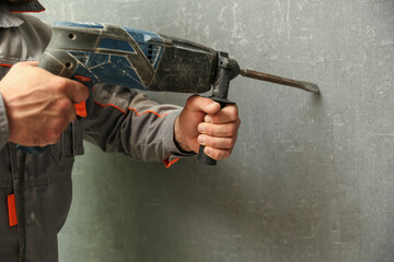 person holds hammer drill close up on gray wall background