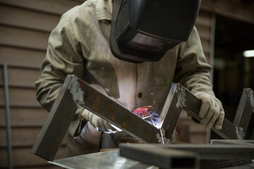 welder welds a metal structure in a workshop with electrical welding