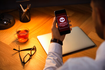 Man holding smartphone with warning about virus attack at table, closeup