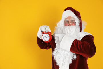 Fototapeta na wymiar Santa Claus holding alarm clock on yellow background, space for text. Christmas countdown