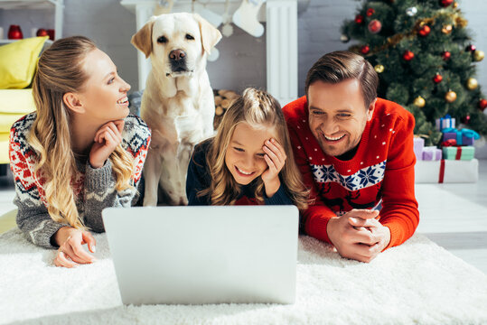 happy family laughing while watching movie on laptop near dog on christmas