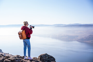 Female tourist taking photo of nature landscape while standing on edge of cliff on