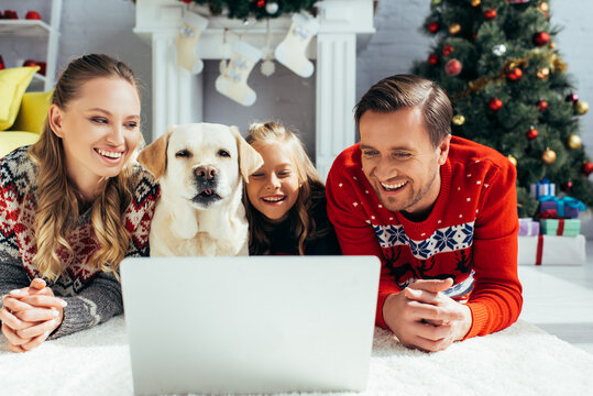 joyful parents watching movie on laptop near daughter and dog on christmas