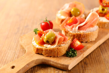 tapas- bread slice with cheese, prosciutto and olive