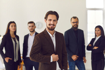 Young business leader or company manager in formal suit with team of office workers in background