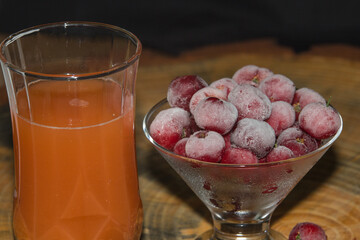 Ready acerola juice with frozen acerolas on the side. vibrant and natural colors. Rich in vitamin C, natural and healthy. rustic wooden table with black background.