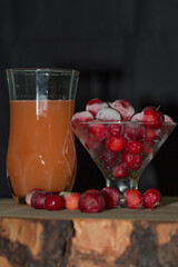 Ready acerola juice with frozen acerolas on the side. vibrant and natural colors. Rich in vitamin C, natural and healthy. rustic wooden table with black background.